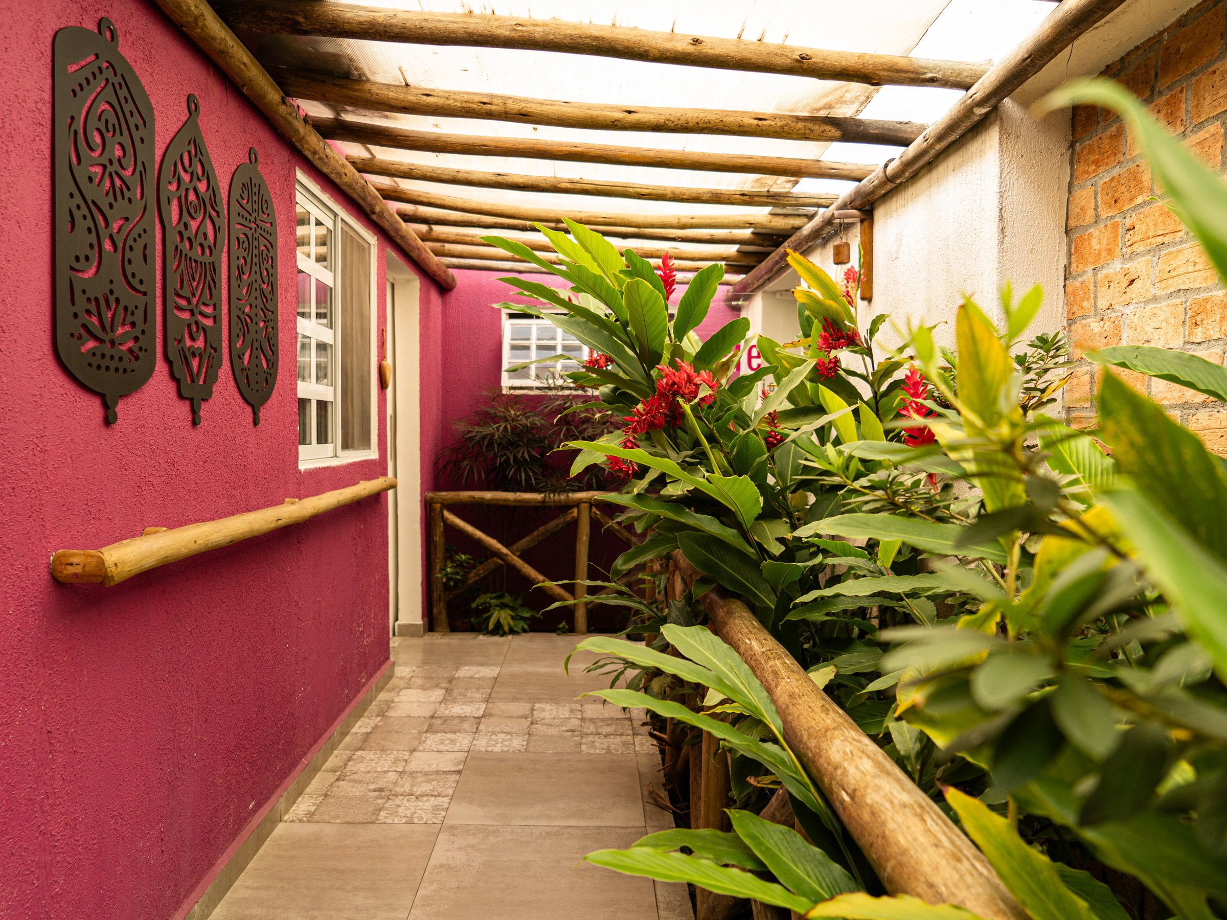 Corredor coberto da La Vie, com parede magenta, plantas e corrimão