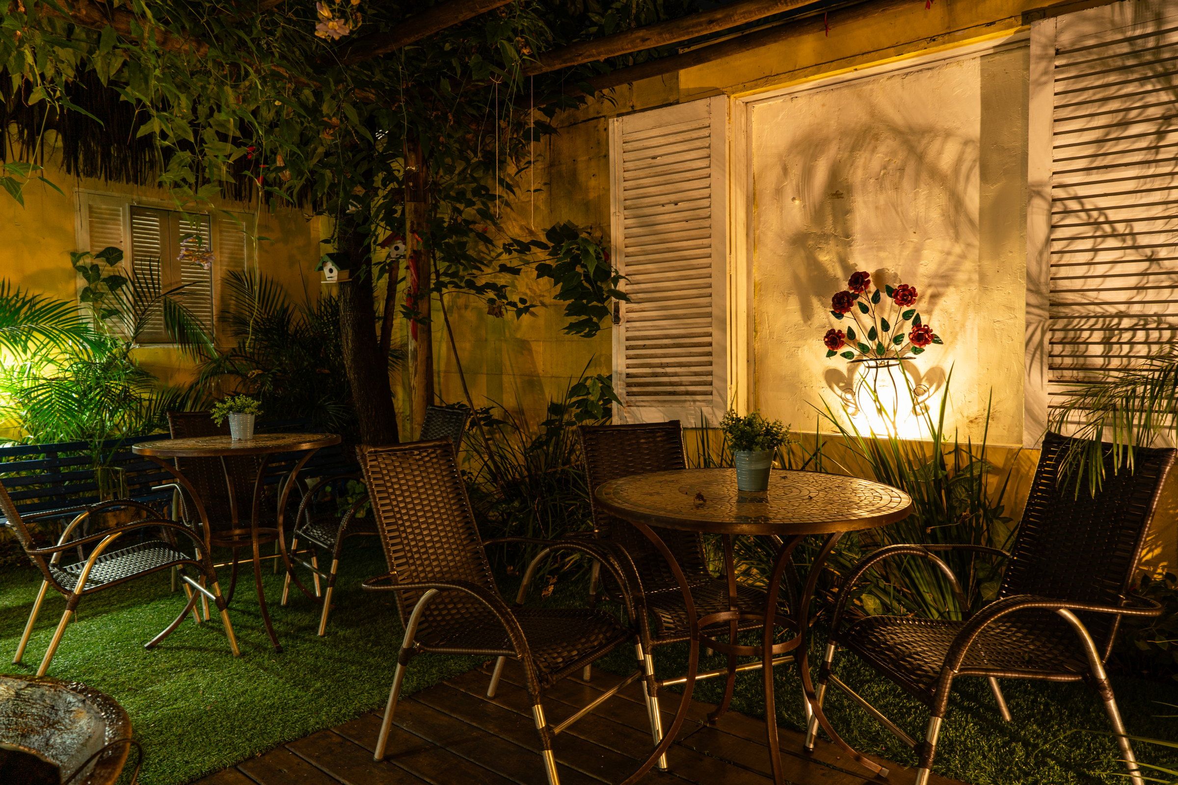 Mesas e cadeiras no deck da Kûara à noite, com luz quente na parede amarela