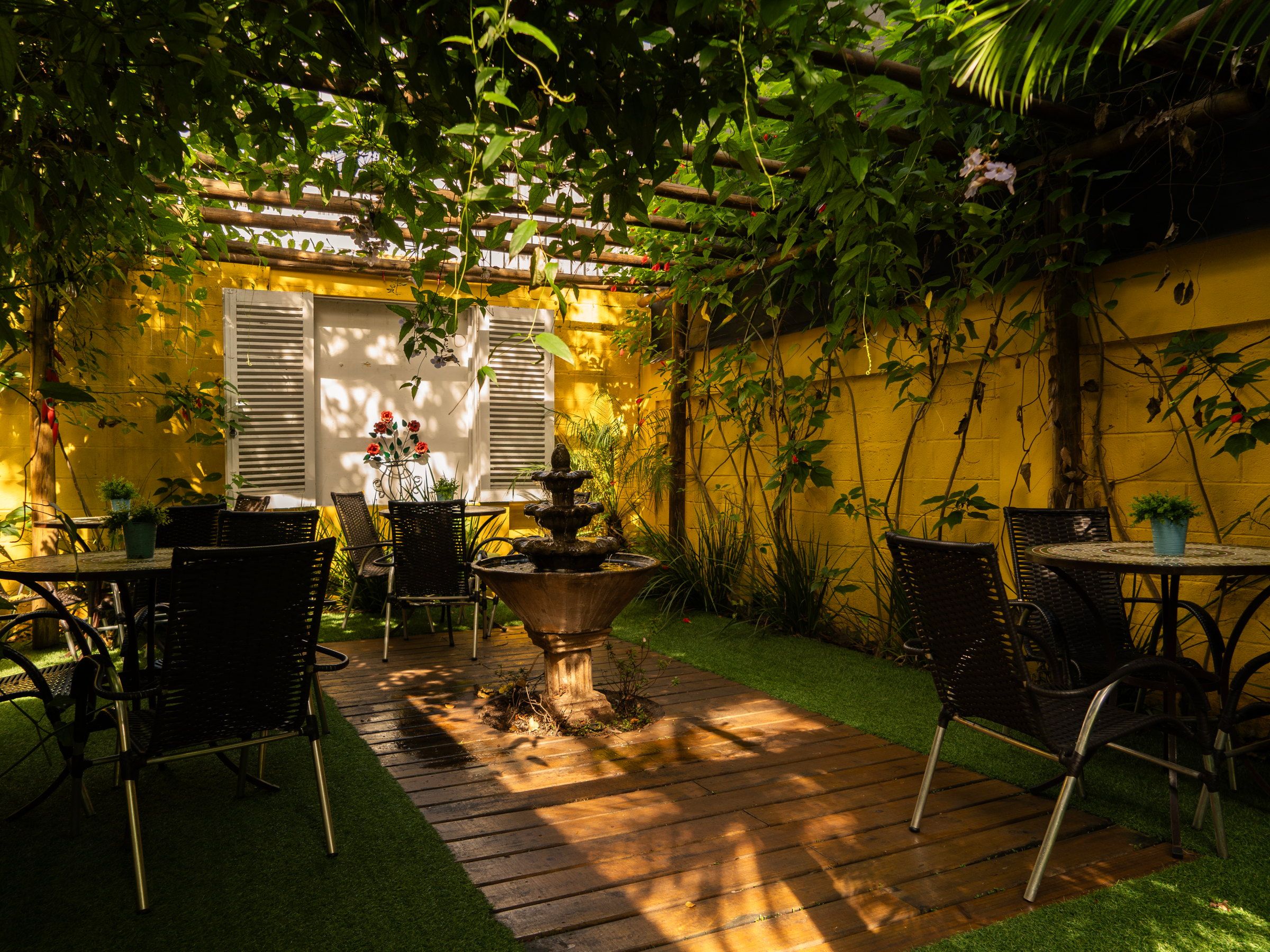 Deck de madeira sob o pergolado da Kûara, com mesas e cadeiras