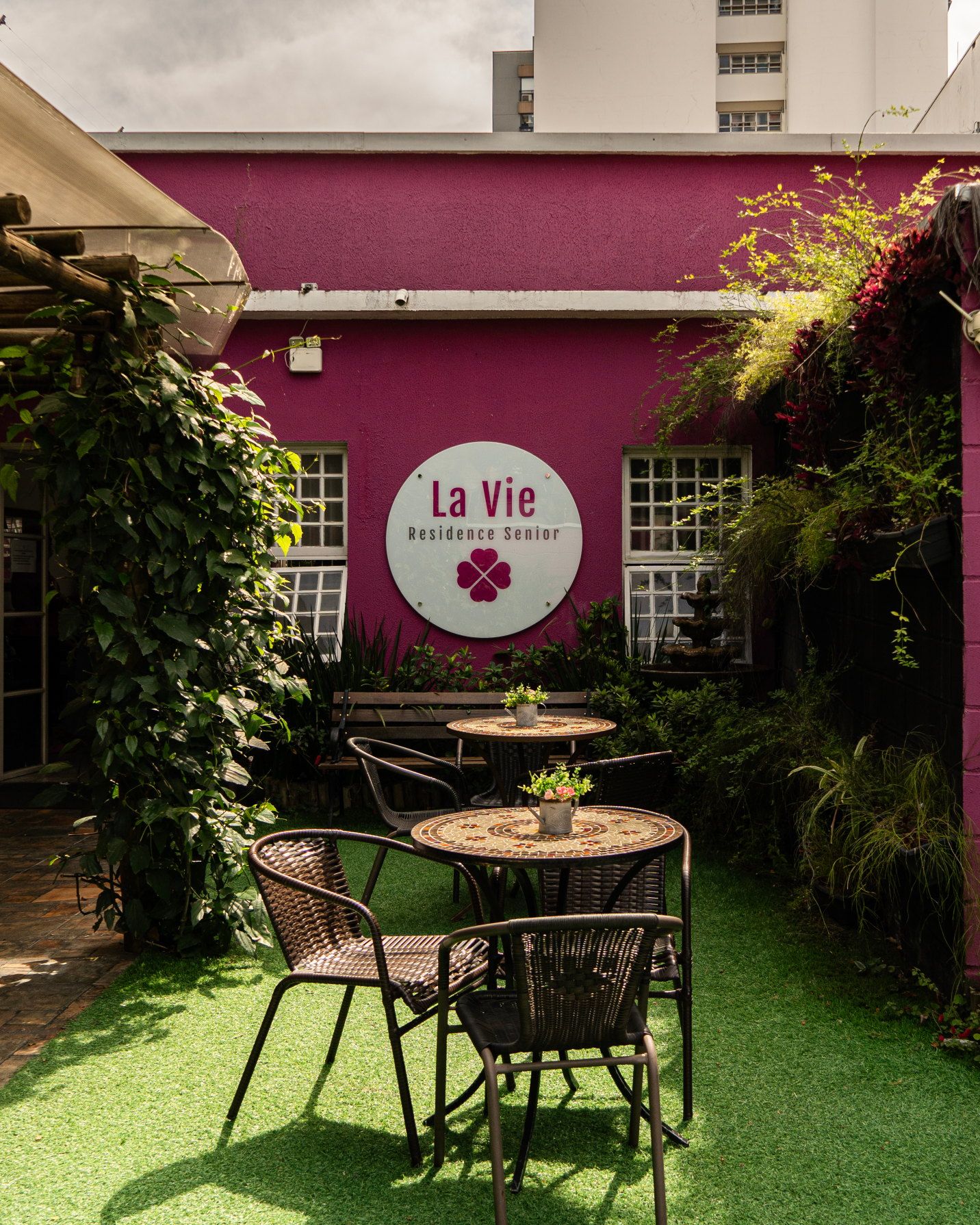Jardim da La Vie com a placa na parede magenta, mesa e cadeiras