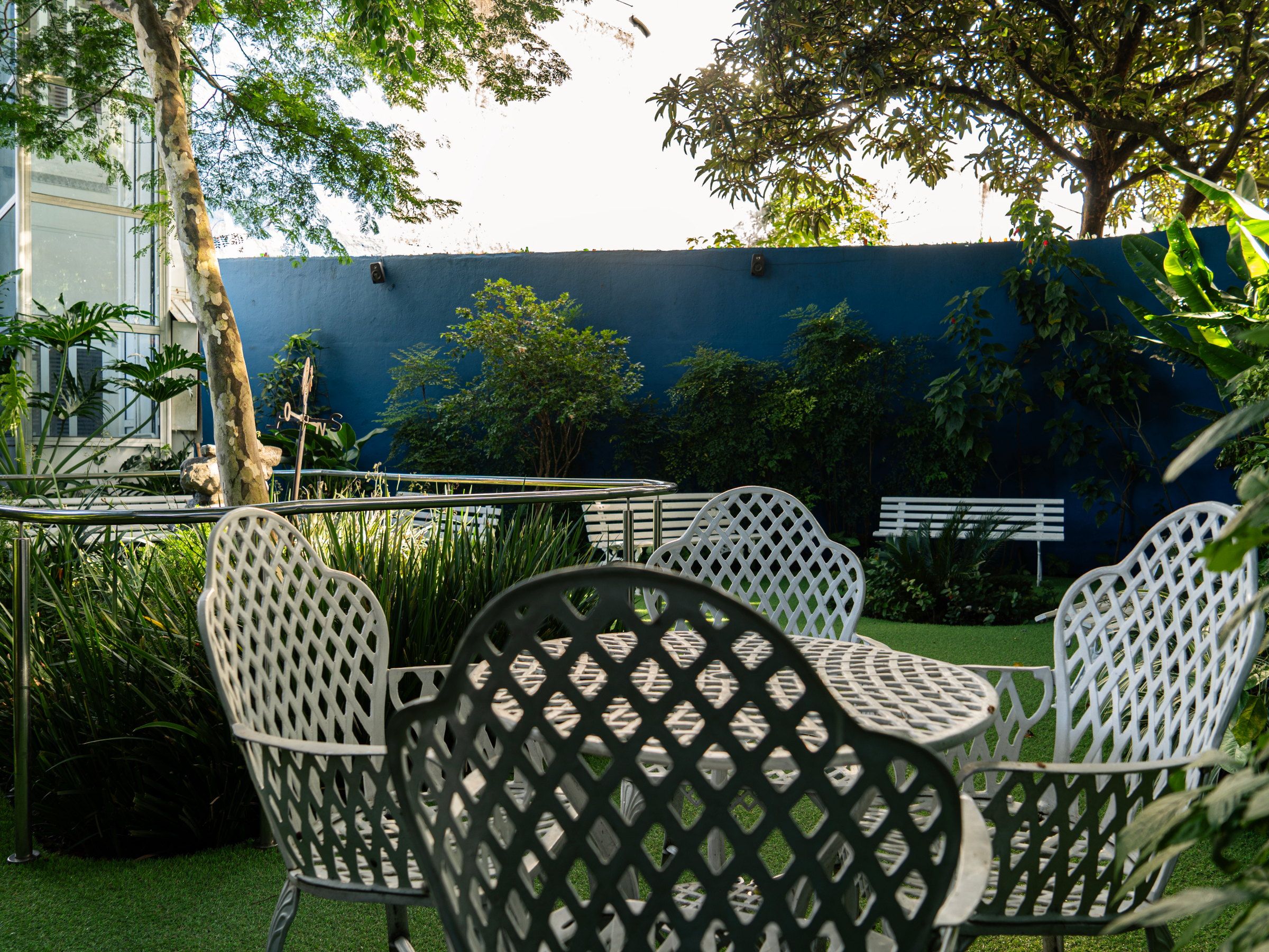 Mesa e cadeiras brancas no jardim do Residencial Espaço Saúde, junto ao muro azul