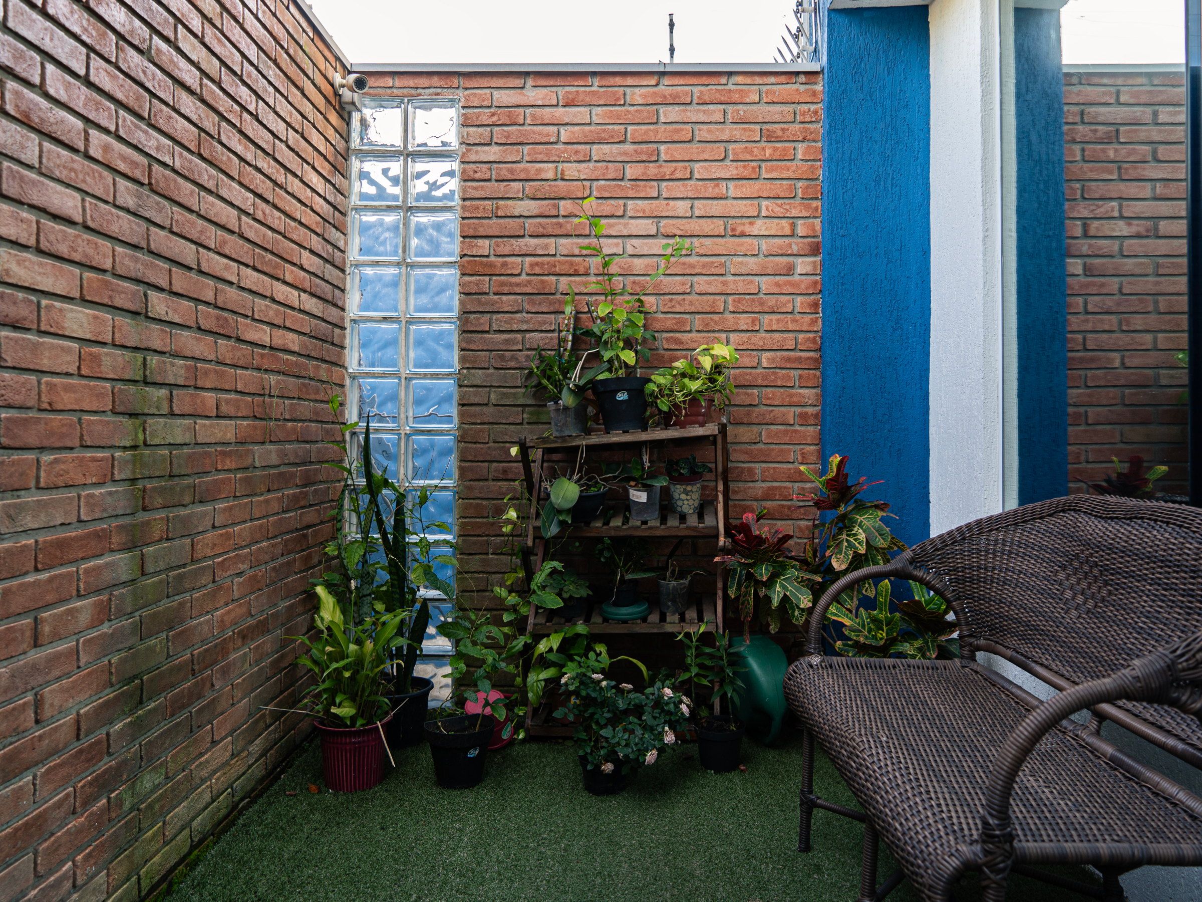 Pátio de tijolo à vista do Residencial Espaço Saúde, com plantas e poltronas