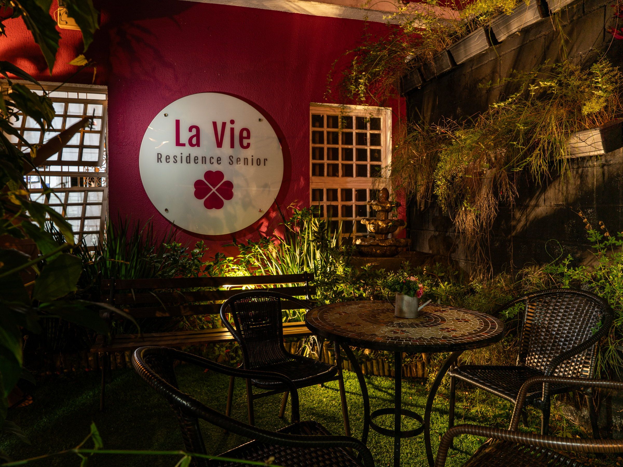 Placa da La Vie iluminada à noite, com mesa e cadeiras no jardim