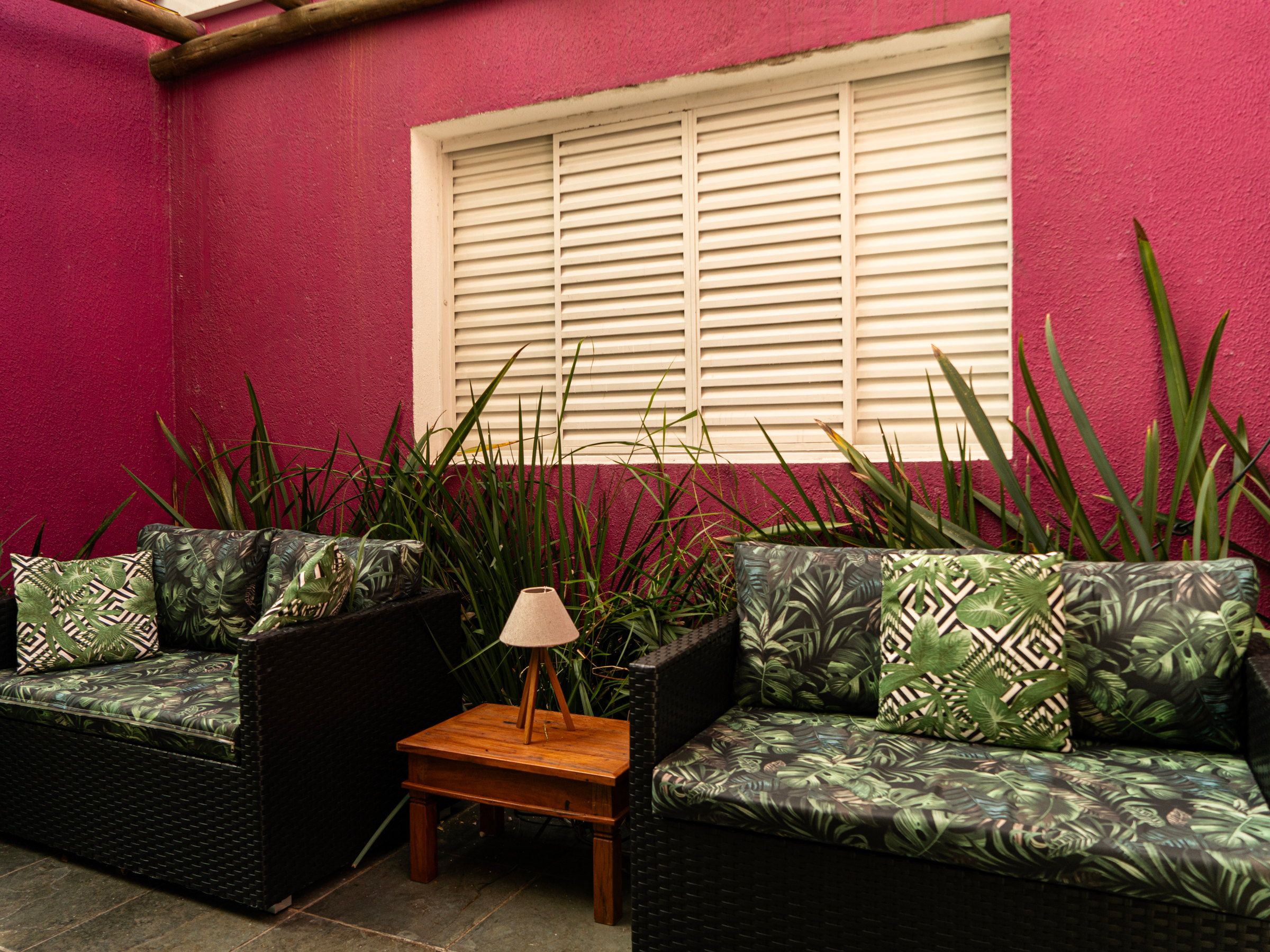 Sofá com almofadas na sala da La Vie, junto à janela e à parede magenta